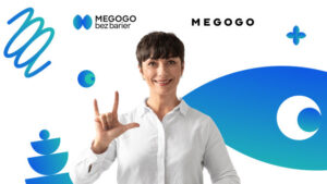 Uśmiechnięta kobieta w białej koszuli pokazuje swoją ręką znak ILY. W tle abstrakcyjne niebieskie elementy graficzne oraz tekst MEGOGO bez barier.