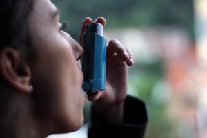 Profil kobiety, która aplikuje sobie inhalator do ust