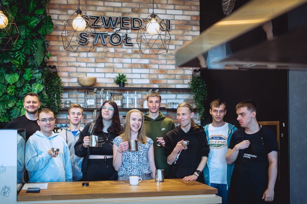 Zdjęcie grupowe przed ladą restauracji. Za grupą na ścianie wisi napis: Szwedzki Stół