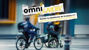 Rozmyte tło ulicy miasta, na którym widać dwie osoby z kaskami na głowach - jedna poruszająca się na rowerze, a druga na wózku inwalidzkim z elektryczną przystawką. Pośrodku znajduje się napis w języku francuskim: Omni Livery. Hacker la plateforme de livraison n 1 pour faire changer le regard sur le handicap.