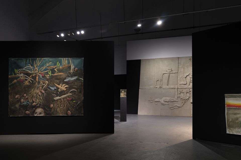 Wnętrze galerii sztuki o przyćmionym oświetleniu. Na ścianach widoczne są trzy prace artystyczne.