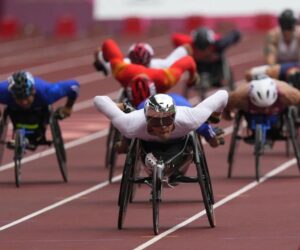 Sportowcy na trójkołowych wózkach na torze stadionowym.