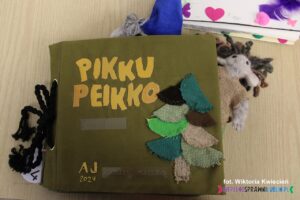 Okładka książki dotykowej pt. "Pikku Peikko" ma naszytą choinkę wykonaną z kolorowych materiałów o grubym splocie