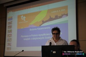 Pani Bożena Kazanowska; w tle ekran ze slajdem tytułowym prezentacji "Pierwsza w Polsce wysyłkowa biblioteka książek z dotykowymi ilustracjami"