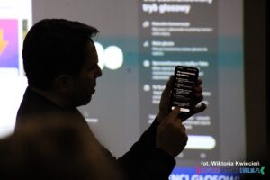 Prowadzący prezentuje zaawansowany tryb głosowy na ekranie smartfona, podczas warsztatu pt. "Sztuczna inteligencja – szanse i zagrożenia dla NGO"