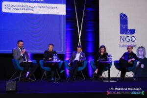 Na fotelach ustawionych w rzędzie siedzą Uczestnicy debaty eksperckiej pt. "Każda organizacja pozarządowa powinna zarabiać"