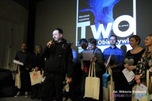 Pan Konrad Drobek z mikrofonem, tuż za Nim w rzędzie stoją pozostali Uczestnicy konkursu