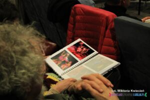 Album ze zdjęciami nadesłanymi na konkurs leży na kolanach jednego z widzów na widowni