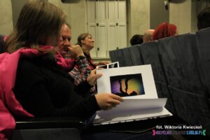 Osoby na widowni oglądają album ze zdjęciami nadesłanymi na konkurs