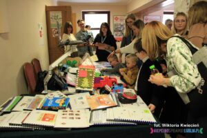 Wiele osób w różnym wieku, zgromadzonych wokół stoiska prezentującego pomoce wspomagające komunikację alternatywną