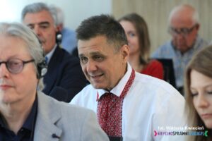 Mężczyzna w białej koszuli ozdobionej tradycyjnym ukraińskim haftem zadaje pytanie do trzymanego przez siebie mikrofonu