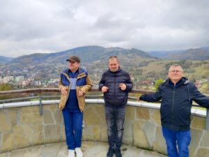 Trzech mężczyzn pozuje w punkcie widokowym; w tle krajobraz gór