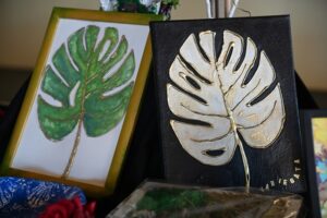 Dwa oprawione dzieła sztuki przedstawiające duże liście. Pierwszy liść jest zielony z żółtą obwódką, a drugi jest biało-złoty na czarnym tle