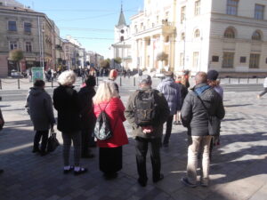 Grupa ludzi stoi na ulicy, naprzeciwko Ratusza i ulicy Krakowskie Przedmieście