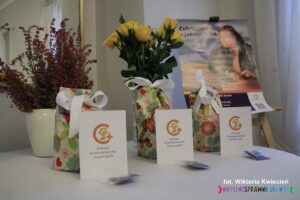 Na niewielkim stoliku ustawiono kwiaty oraz przygotowane do wręczenia odznaki, legitymacje i małe upominki, w tle wyeksponowano plakat "Cukrzyca a jakość życia"