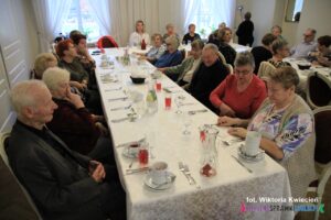 Przy zastawionym stole nakrytym białym obrusem siedzą uczestnicy spotkania z okazji obchodów Światowego Dnia Cukrzycy