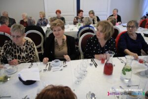 Goście siedzący przy stole w oczekiwaniu na obiad; na pierwszym planie cztery kobiety