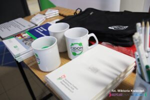 Na pierwszym planie znajdują się notesy i kubeczki promujące CIDON