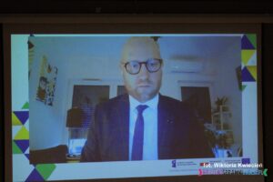 Pan Filip Maciągowski, Przedstawiciel Ministerstwa Funduszy i Polityki Regionalnej podczas połączenia online wyświetlonego na ekranie multimedialnym