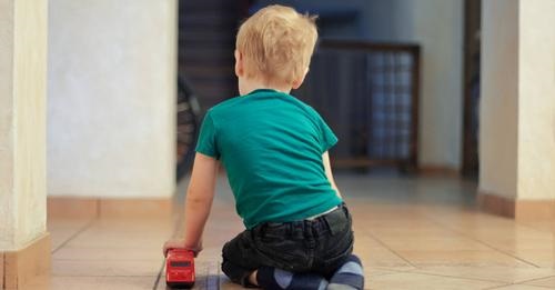 Dziecko w zielonej koszulce siedzi na podłodze i bawi się czerwonym samochodzikiem