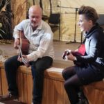 Na scenie siedzą Pan Robert Kozak wraz z Karoliną Czajką,, obydwoje trzymają gitary,