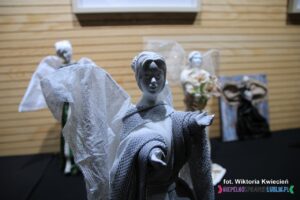 Biało-szara figurka Anioła z wyciągniętymi do przodu rękami, wykonana w SDS w Górze Puławskiej w ramach warsztatów“Cementowo – Powertexowe wariacje aniołowe” – instruktor: Joanna Rodzoch,