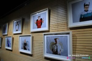 Na ścianie wiszą fotografie w białych ramach, wykonane w ŚDS "Absolwent" w ramach warsztatów “Anioły w obiektywie” – instruktor: Aneta Antosik, Emilia Pluta