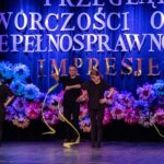 Trzy kobiety i jeden mężczyzna w czarnych strojach wykonują ruchy, które wprawiają w obrót żółte wstążki.