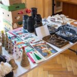 Stół z eksponowanymi ręcznie robionymi wyrobami, w tym stożkowate choinki, dekoracyjne wazony i świąteczne kartki z życzeniami.