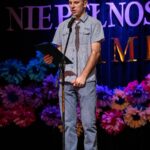 Mężczyzna na scenie śpiewa do mikrofonu, trzymając w ręku tekst piosenki.