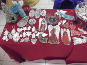 Stół z różnorodnymi dekoracjami bożonarodzeniowymi, w tym figurkami aniołów i ozdobami choinkowymi.