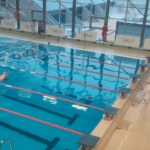 Perspektywa z trybuny na zawodników pływających w stronę mety.