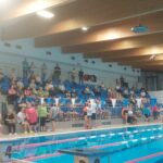 Tłum dorosłych i dzieci ogląda wydarzenie znad trybun, niektórzy stoją, a inni siedzą.