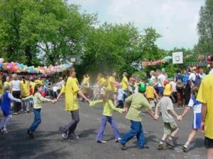 Zabawa integracyjna na boisku, dzieci w różnym wieku trzymając się za ręce poruszające się po okręgu