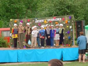 Na scenie w plenerze stoi dziesięcioosobowa grupa dzieci, częściowo zasłaniają one napis w tle "Dzień Godności Osoby z Niepełnosprawnością"