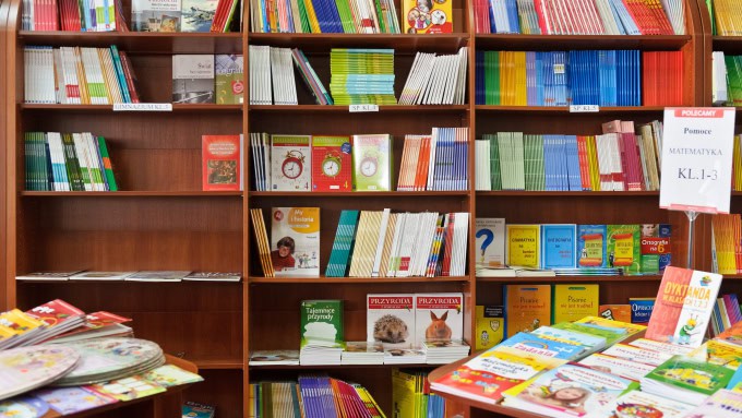 Półki na książki wypełnione kolorowymi książkami i materiałami edukacyjnymi w księgarni. Na stołach ekspozycyjnych znajdują się różne książki dla dzieci.