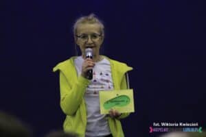 Kobieta w średnim wieku trzyma w ręku voucher na Nordikiadę 2025 - rajdy z kijkami do nordic walking