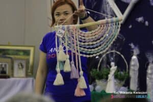 Kobieta prezentuje licytowaną ozdobę wykonaną techniką makramy