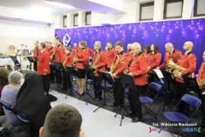 Na scenie prezentuje się Orkiestra Dęta Gminy Końskowola. Muzycy ubrani są w jednakowe czerwono-czarne mundury