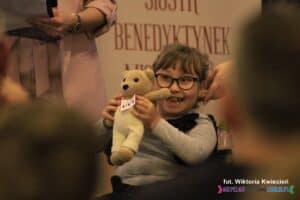 Licytowana maskotka misia wykonana na szydełku, prezentowana przez roześmianą właścicielkę