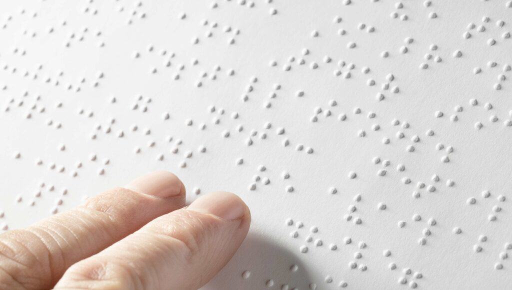 Palce dotykają tekstu zapisanego w brajlu.