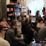 We wnętrzu księgarni siedzi duża grupa osób; w tle półki z książkami