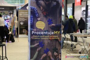 Pionowy baner akcji ProcentujeMY ustawiony w przestrzeni centrum handlowego SKENDE