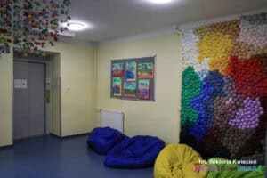 Na korytarzu znajduje się winda do przewozu osób z niepełnosprawnością ruchową; po prawej stronie ścianka sensoryczna składająca się z miękkich kolorowych kulek - autorem projektu jest Paweł Totoro Adamiec