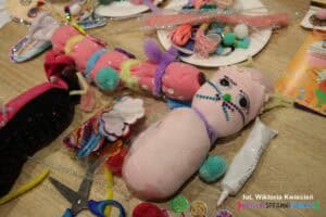 Na drewnianym blacie, pomiędzy materiałami pasmanteryjnymi, leżą maskotki wykonane z wypchanych skarpetek – dżdżownica i kot
