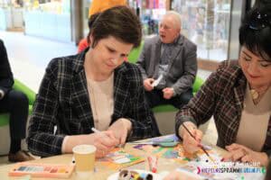 W warsztatach plastycznych uczestniczyła Pani Joanna Olszewska, Pełnomocnik Prezydenta do Spraw Osób Niepełnosprawnych. Na zdjęciu siedzi przy stole i maluje farbami zakładkę w kształcie skarpetki