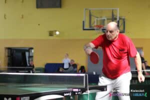 Zawodnik z WTZ Nałęczów w czerwonej koszulce trzyma rakietkę w prawej ręce w gotowości do przyjęcia nadlatującej piłki. Zawodnik jest w dynamicznej pozycji, skupiony na nadchodzącej akcji