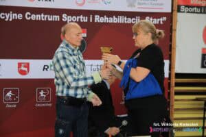 Pani Agnieszka Barszczyk wręcza puchar Panu Aleksandrowi Rudzińskiemu za zajęcie I miejsca w kategorii V: osoby z niepełnosprawnością ruchową bez klasyfikacji sportowej