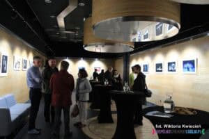 We foyer sali LCK zgromadziły się grupy osób. W tle, na ścianach wiszą dobrze doświetlone reflektorami fotografie