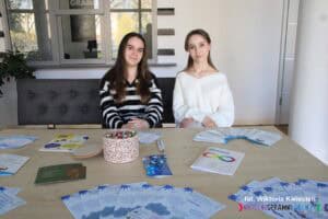 Dwie młode kobiety siedzą przy stoliku Akademickiego Centrum Wsparcia UMCS, przed nimi rozłożono materiały informacyjne